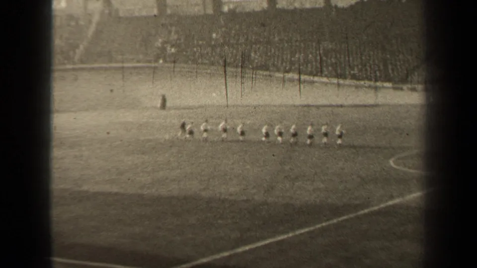 Distant 1947 Paris stadium view showing football players lined up on the pitch before the match continues.