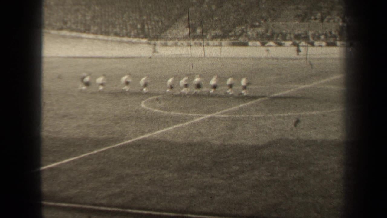 In 1947 Paris footage, a football team in light jerseys jogs across the pitch while spectators sit in the distant stands.