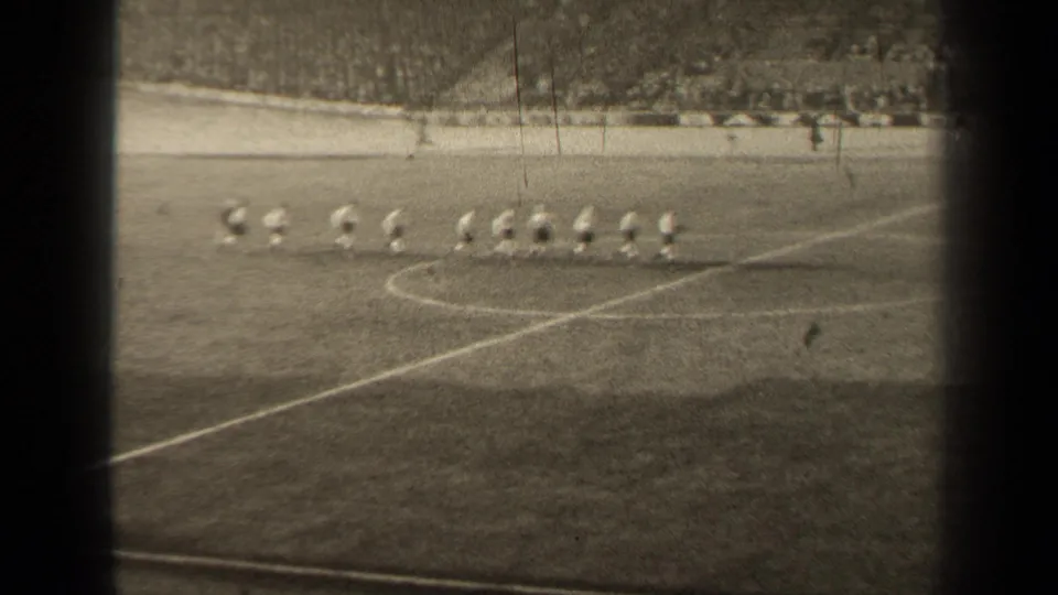 In 1947 Paris footage, a football team in light jerseys jogs across the pitch while spectators sit in the distant stands.