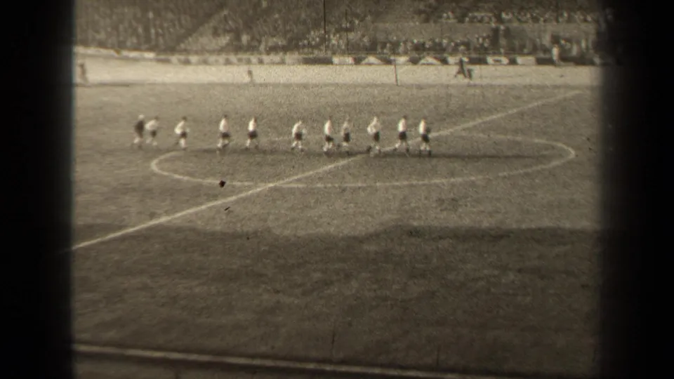 Football players in light tops and dark shorts move in formation across a Paris pitch, with a crowd visible beyond the field.