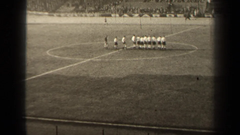 A group of football players clusters near midfield in the Paris 1947 clip, with stands and field markings visible behind them.