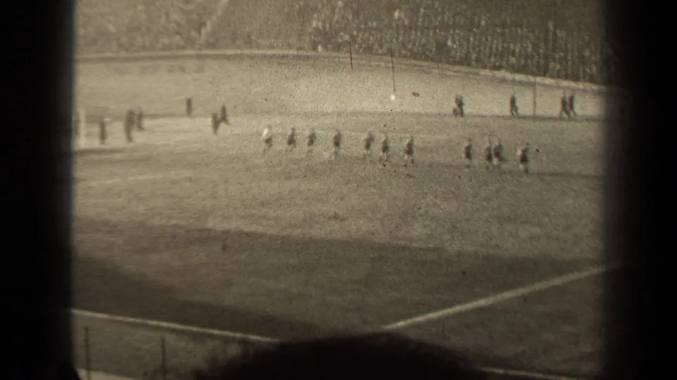 Players in light and dark uniforms cross the pitch in a 1947 Paris soccer scene filmed from the stands.
