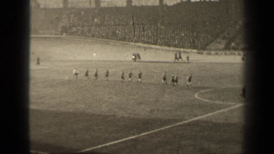 Distant 1947 Paris soccer field view with players spreading into position under bright daylight in black-and-white 8mm footage.