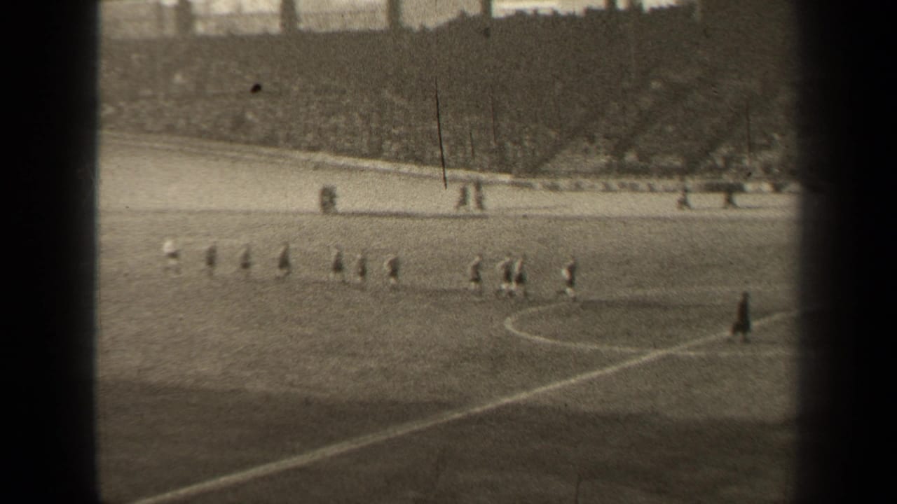 1947 Paris home-movie frame showing soccer players spread across the pitch near the center circle as a packed stadium watches.