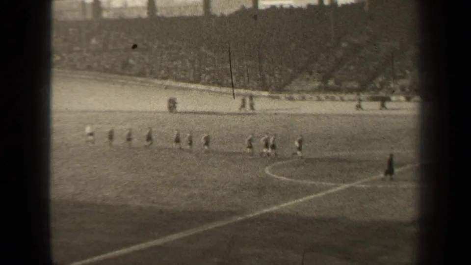 1947 Paris home-movie frame showing soccer players spread across the pitch near the center circle as a packed stadium watches.