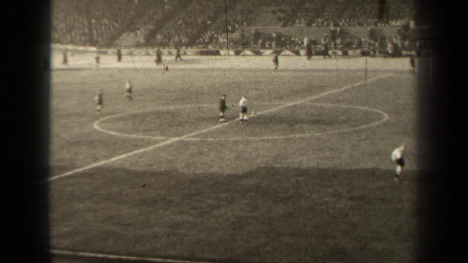 Distant 1947 Paris football scene with players near midfield and a partial player figure entering the lower frame edge.