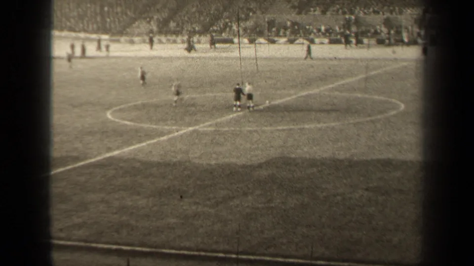 Wide 8mm view of a 1947 football match in Paris, with players grouped near midfield and spectators lining the stands.