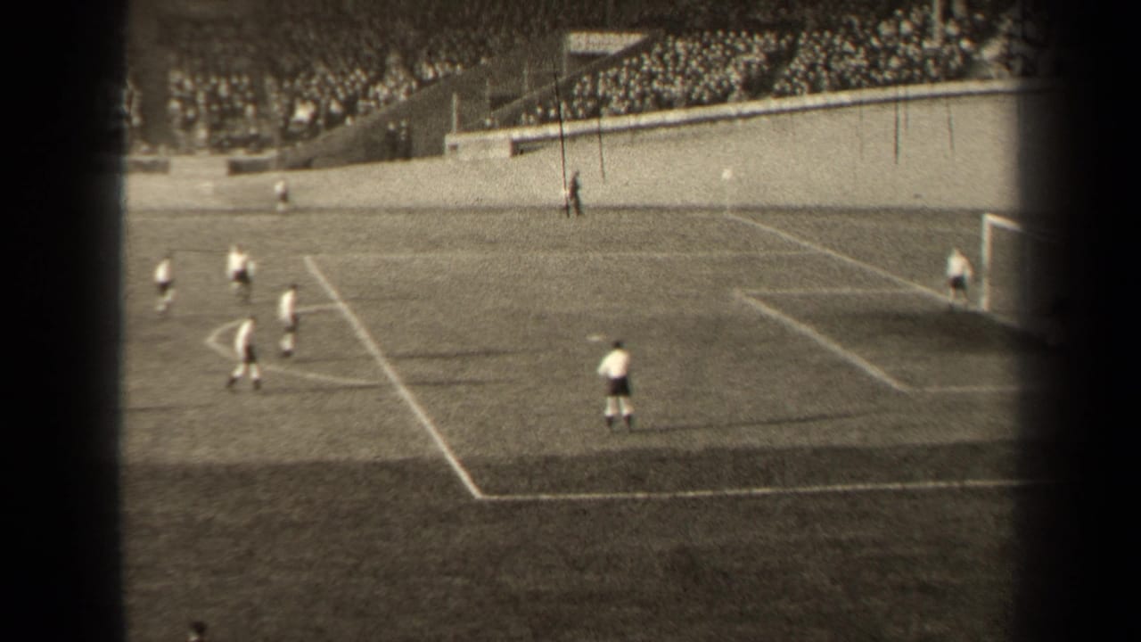 Soccer players in light and dark kits move near the penalty area during a 1947 Paris match, with a large crowd visible behind the field wall.