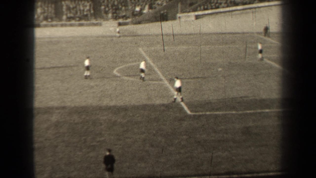 Players in white uniforms move across a marked grass field near the penalty area.