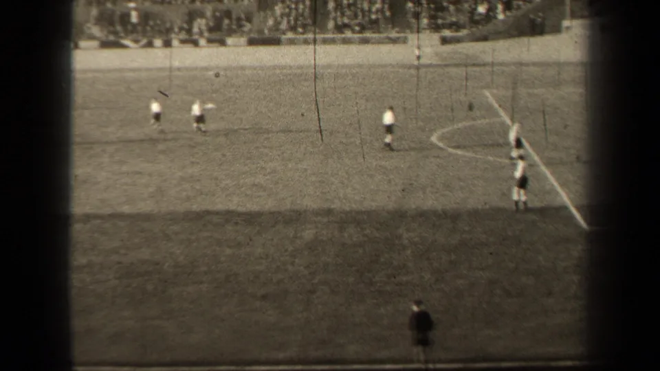 1947 Paris 8mm frame showing a wide field hockey view, with players on the pitch and a dark-clothed figure at the lower sideline.