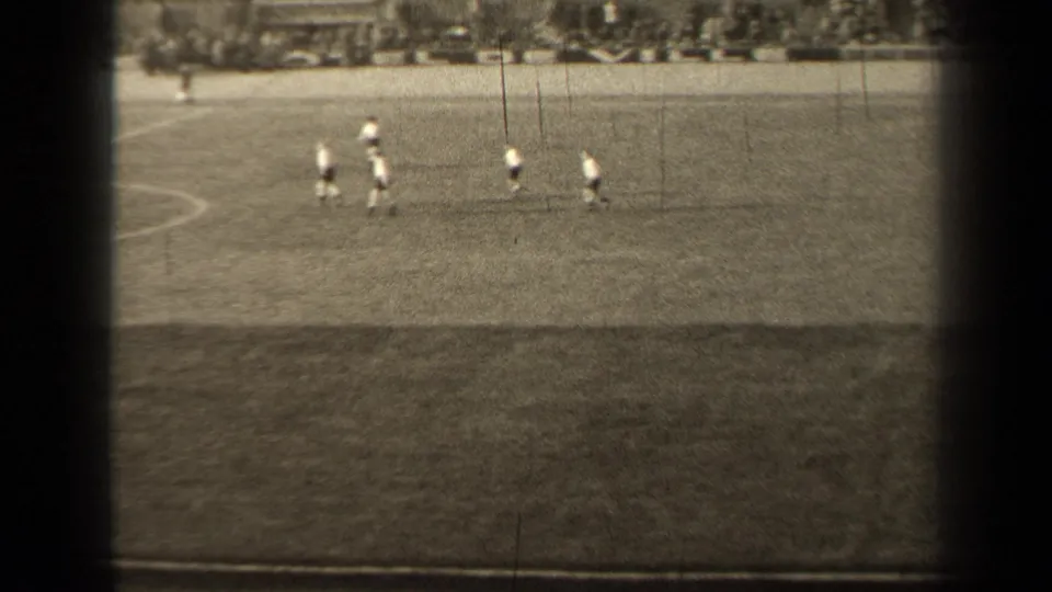 Final 1947 Paris frame with several distant field hockey players grouped on the pitch, seen through dark 8mm frame edges.