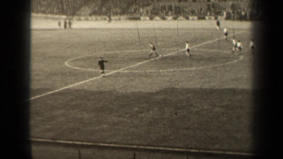 Distant 1947 Paris soccer action near midfield, with several players, a dark-clad official or player, and spectators beyond the pitch.