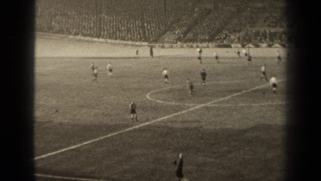 Soccer match in progress with players near midfield and spectators beyond the pitch.