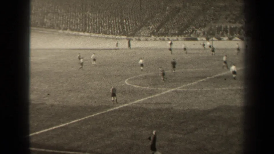 Distant view of a 1947 Paris soccer match, with light and dark uniforms visible against the grass and crowd seating behind.