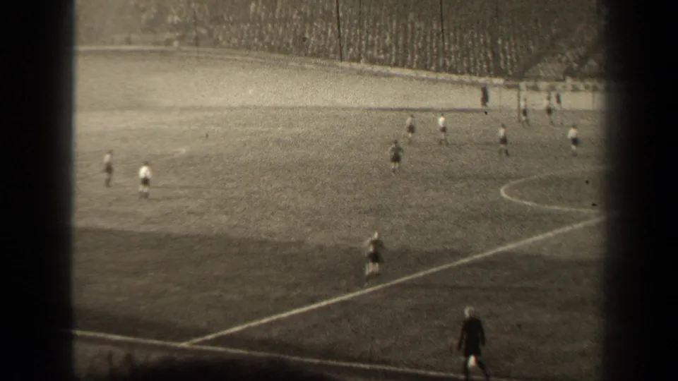 Late frame from the 1947 Paris soccer footage, with players near the far touchline and a dark-uniformed figure closer to camera.