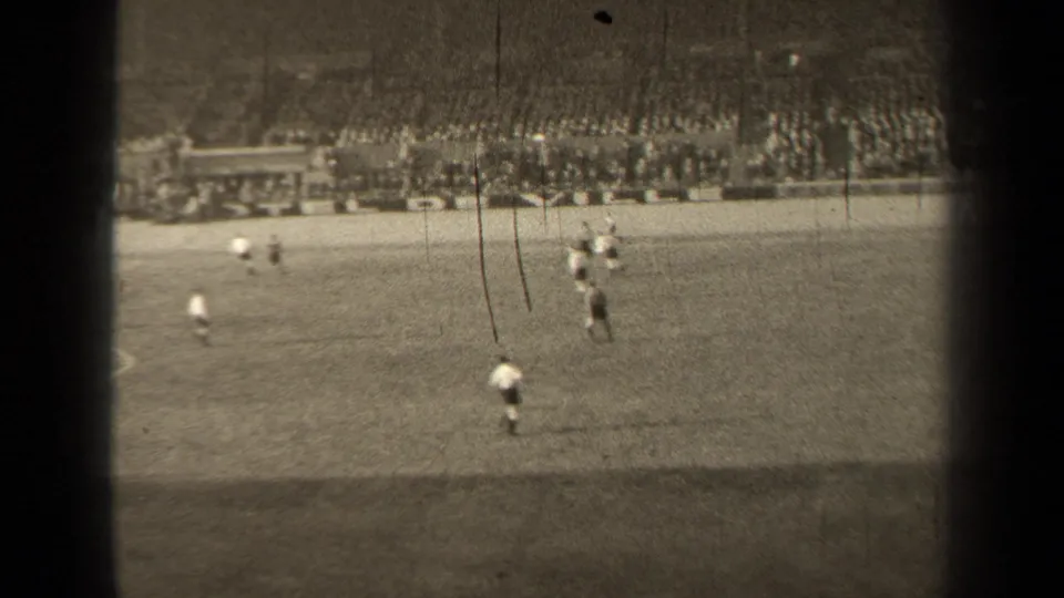 Distant view of a 1947 Paris soccer match, with players clustered near midfield and spectators lining the far stands.