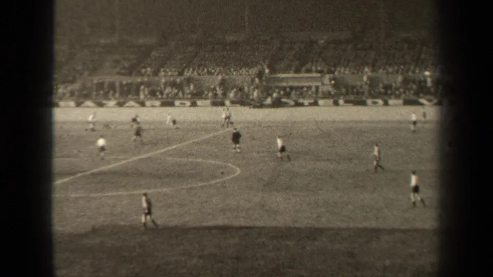 1947 Paris stadium soccer scene with players near the center markings, viewed through grainy 8mm film from a high vantage point.