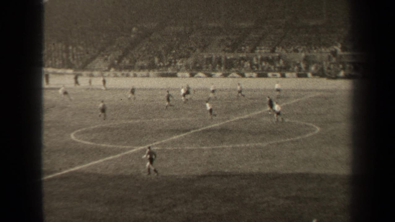 Soccer players run near the center circle with packed stands in the background.