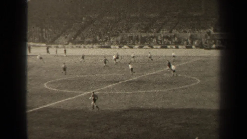 Wide 8mm view of a 1947 Paris soccer match, showing players in contrasting kits near midfield and a dense spectator crowd.