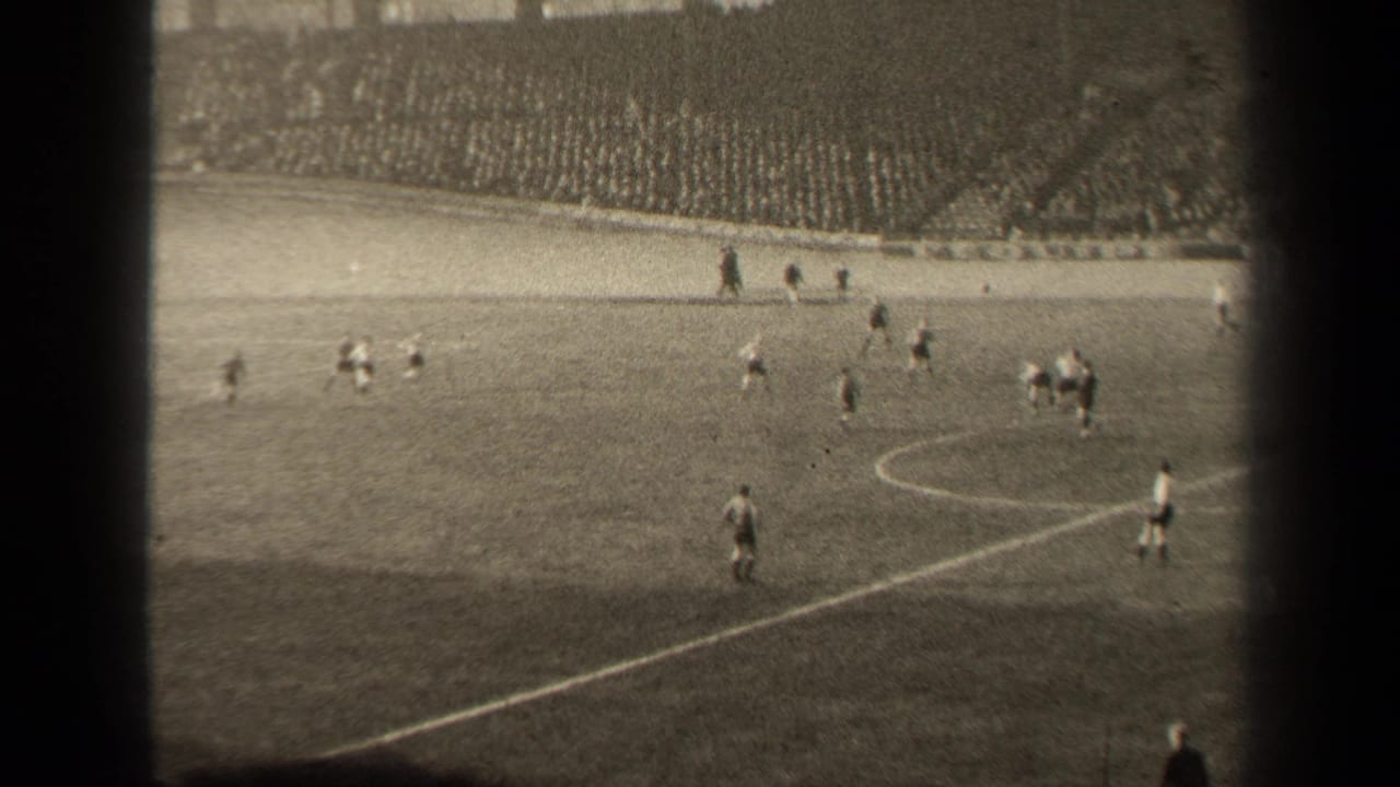1947 Paris 8mm frame showing a wide soccer match view, players in light and dark uniforms, pitch markings and packed stands.