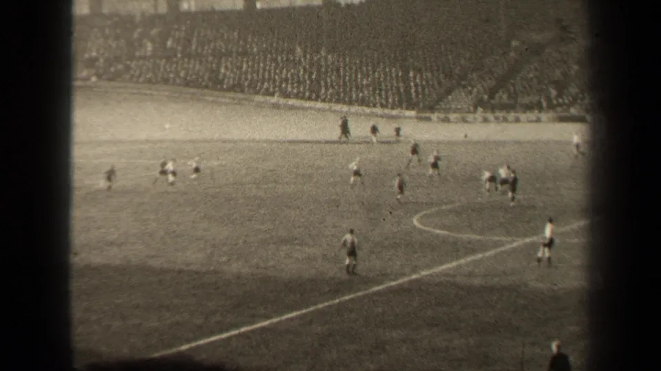 1947 Paris 8mm frame showing a wide soccer match view, players in light and dark uniforms, pitch markings and packed stands.
