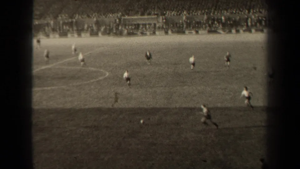 Wide 1947 Paris soccer frame with a runner near the ball, scattered players, field lines and spectators filling the far stands.