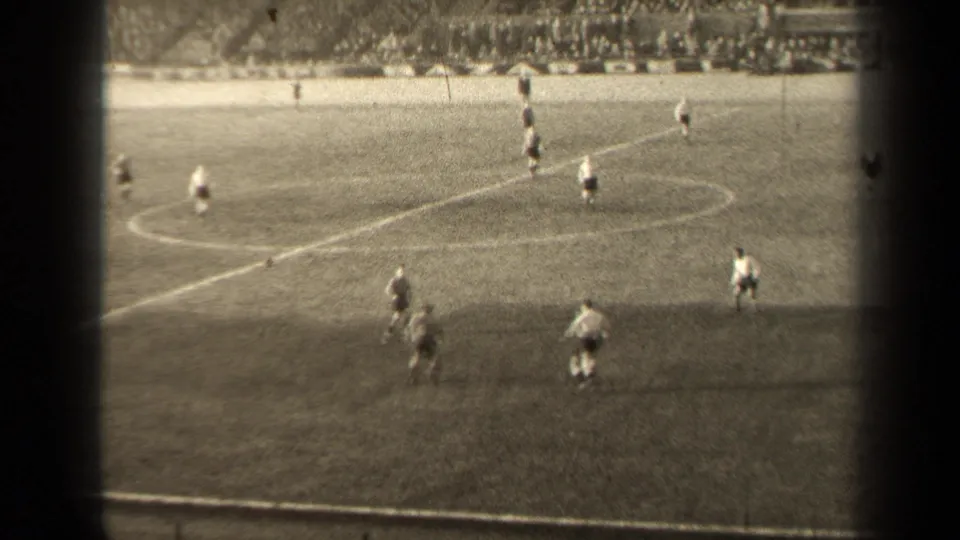 1947 Paris 8mm soccer frame showing players near the center circle, a marked grass field, distant crowd and dark vignetted film edges.