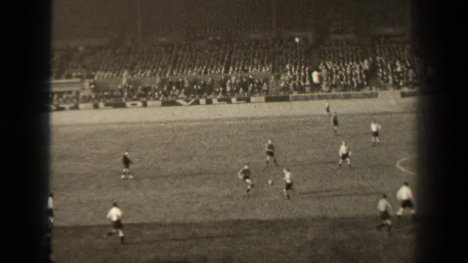Home-movie view of a 1947 Paris soccer match, with several players near the touchline and a packed seating section behind them.