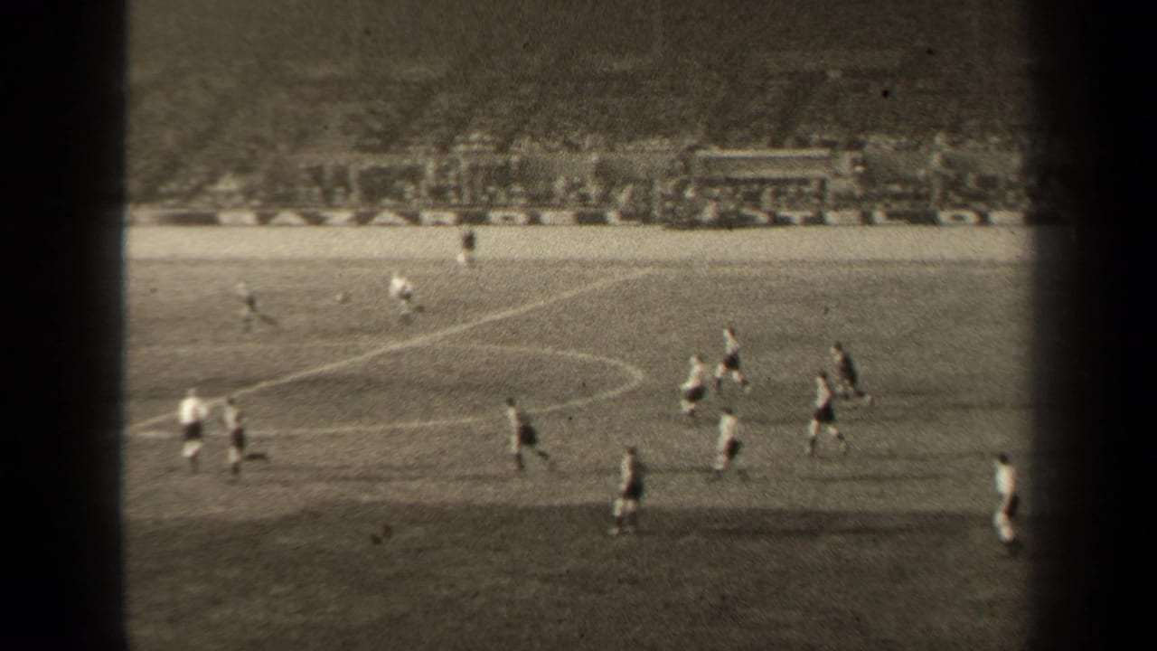 Football players run across the field in front of a crowded stadium stand.