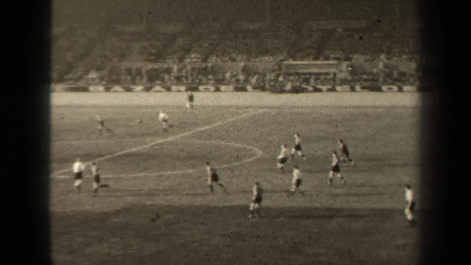 Wide 8mm view of a 1947 Paris football match, with players crossing the pitch and a packed stand behind them.