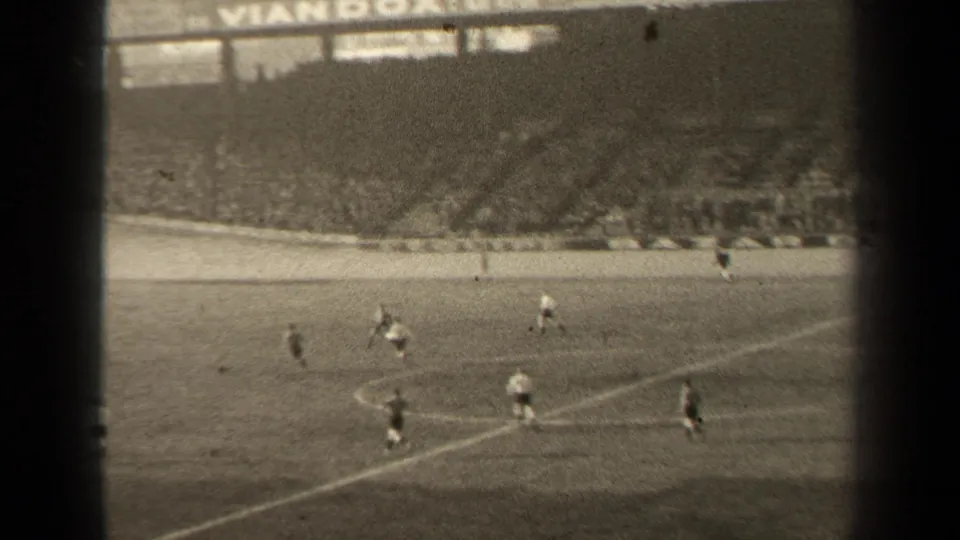 Spectator-shot 1947 Paris football action near the touchline, with players in light and dark kits below the stadium crowd.