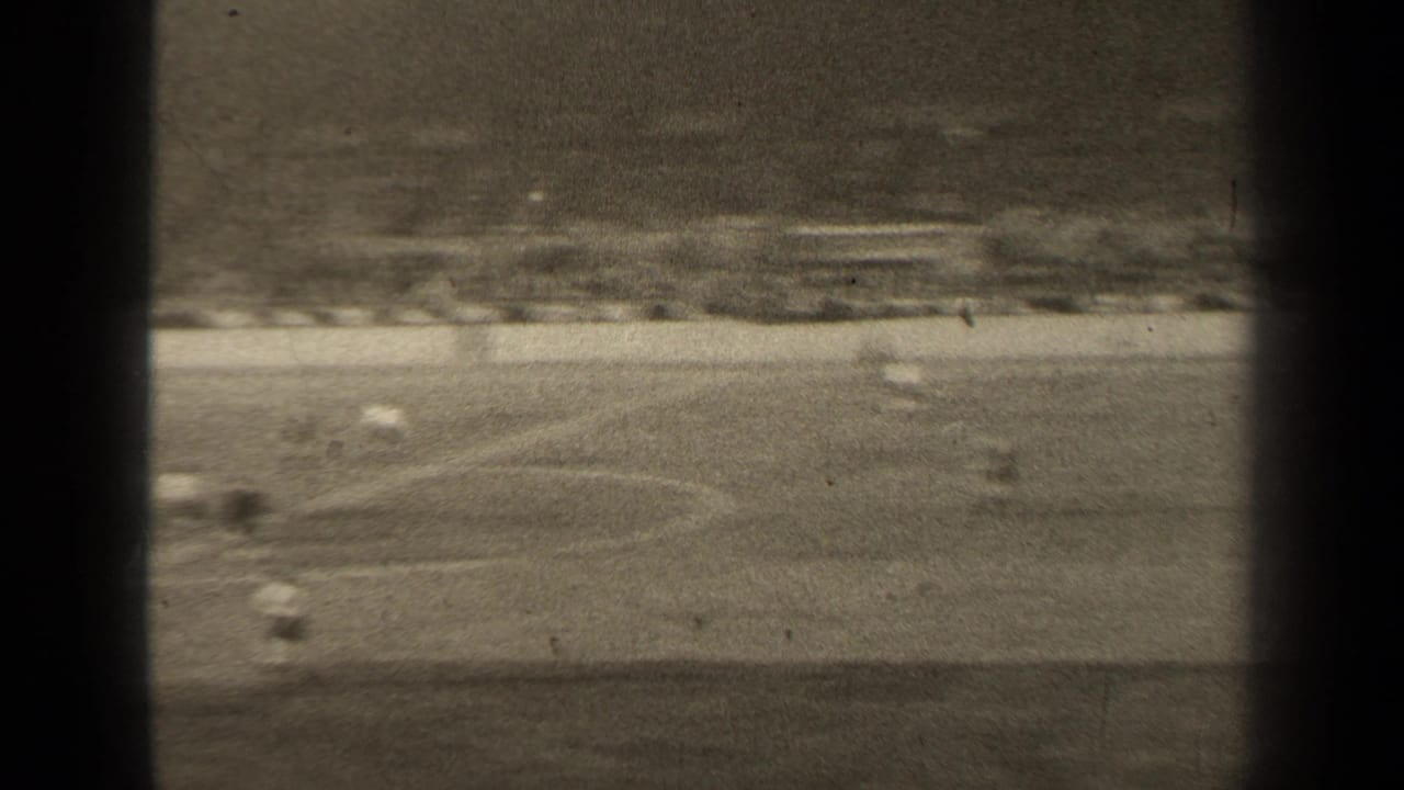 Blurred soccer action across the field with several players and distant stadium seating.