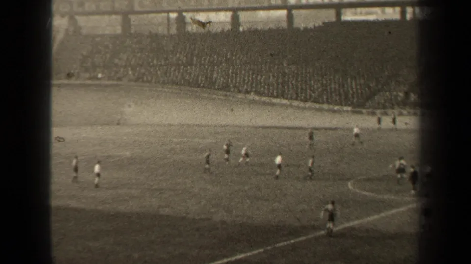 Distant 1947 Paris soccer scene with players near midfield, visible pitch markings, and a dense crowd in the stands.