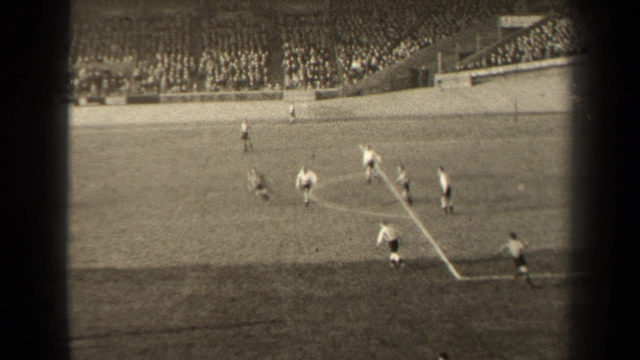 Players cluster near a marked penalty area with spectators in the stands.