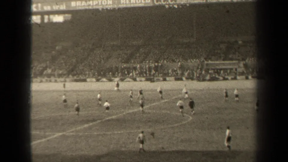 1947 Paris 8mm frame showing a wider soccer match view with players positioned across the field, visible pitch lines, and crowded stadium seating beyond.