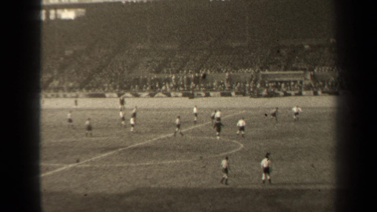 1947 Paris football action seen in a wide 8mm frame, with players in light and dark kits and spectators filling the far stands.