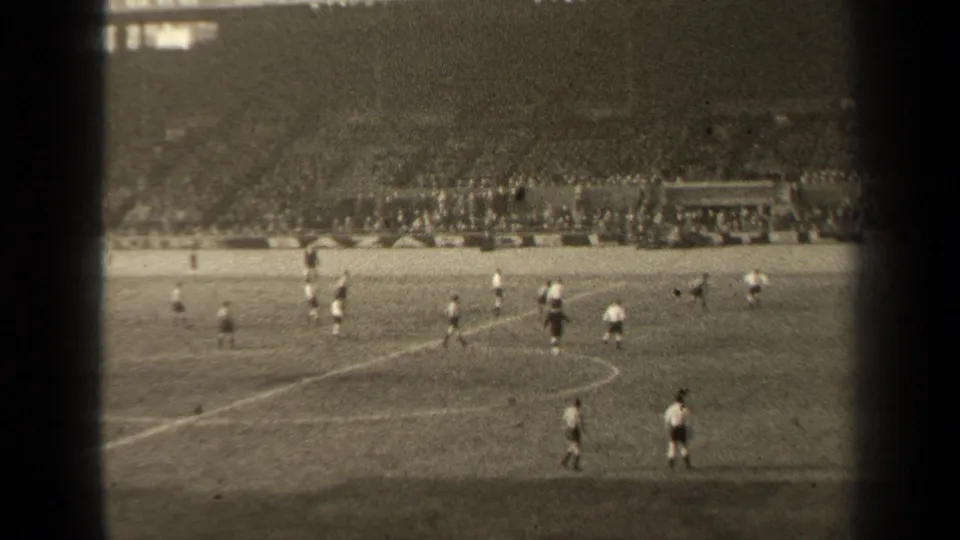 1947 Paris football action seen in a wide 8mm frame, with players in light and dark kits and spectators filling the far stands.