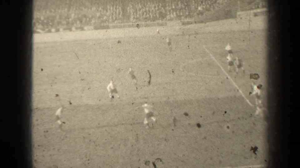 Overexposed 1947 Paris 8mm frame showing football players near the goal area, with field lines and distant spectators faintly visible.