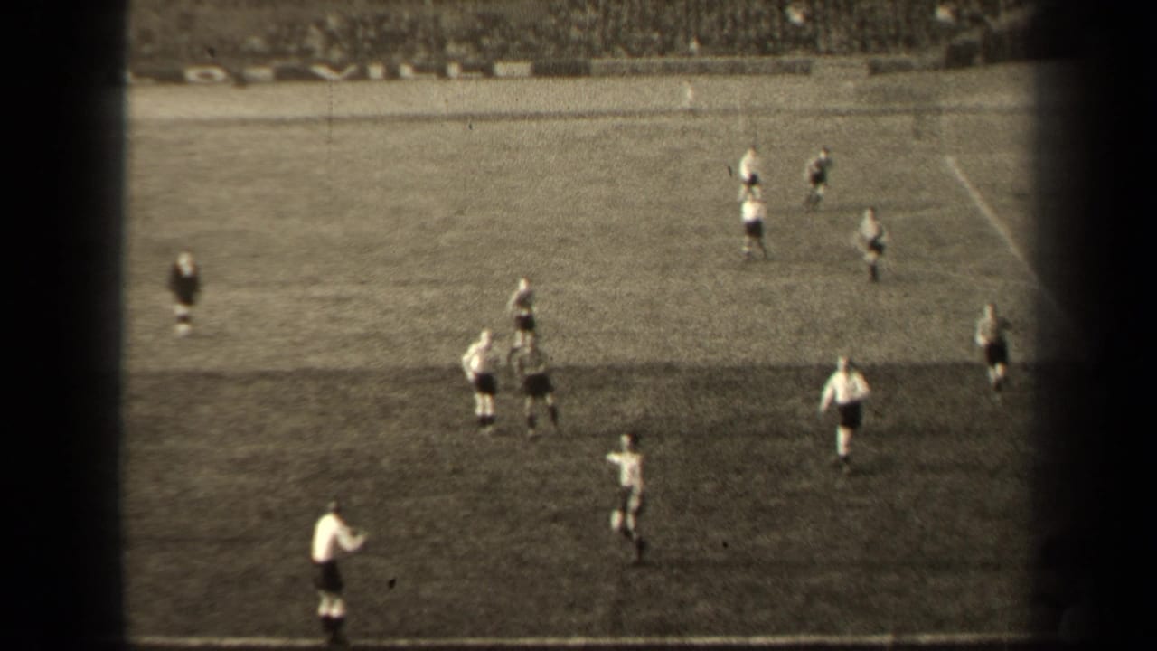 Wide 8mm view of the Paris soccer match, with players spread across the pitch and spectators filling the far stands.