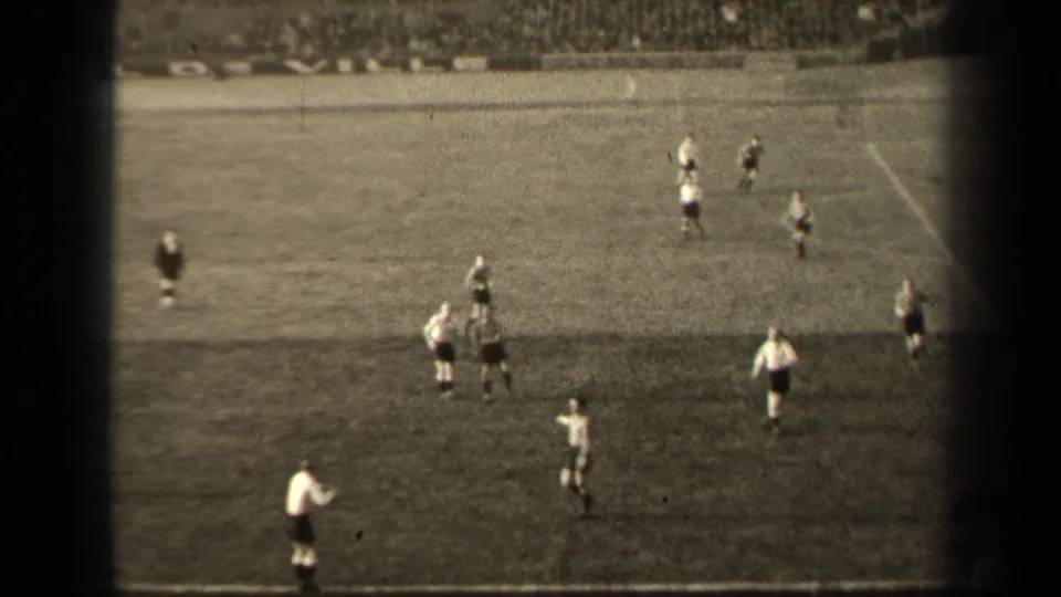 Wide 8mm view of the Paris soccer match, with players spread across the pitch and spectators filling the far stands.