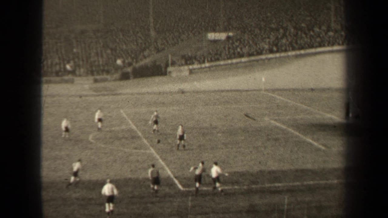 Soccer players on a grass field with stadium spectators in the background.