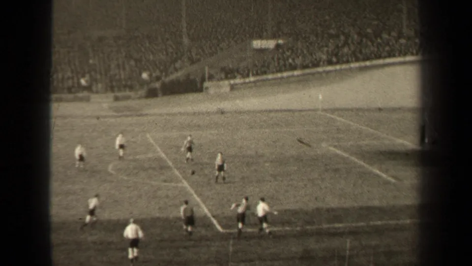 Distant 1947 Paris soccer action seen from a high spectator position, with players near the penalty area and crowded stands behind them.