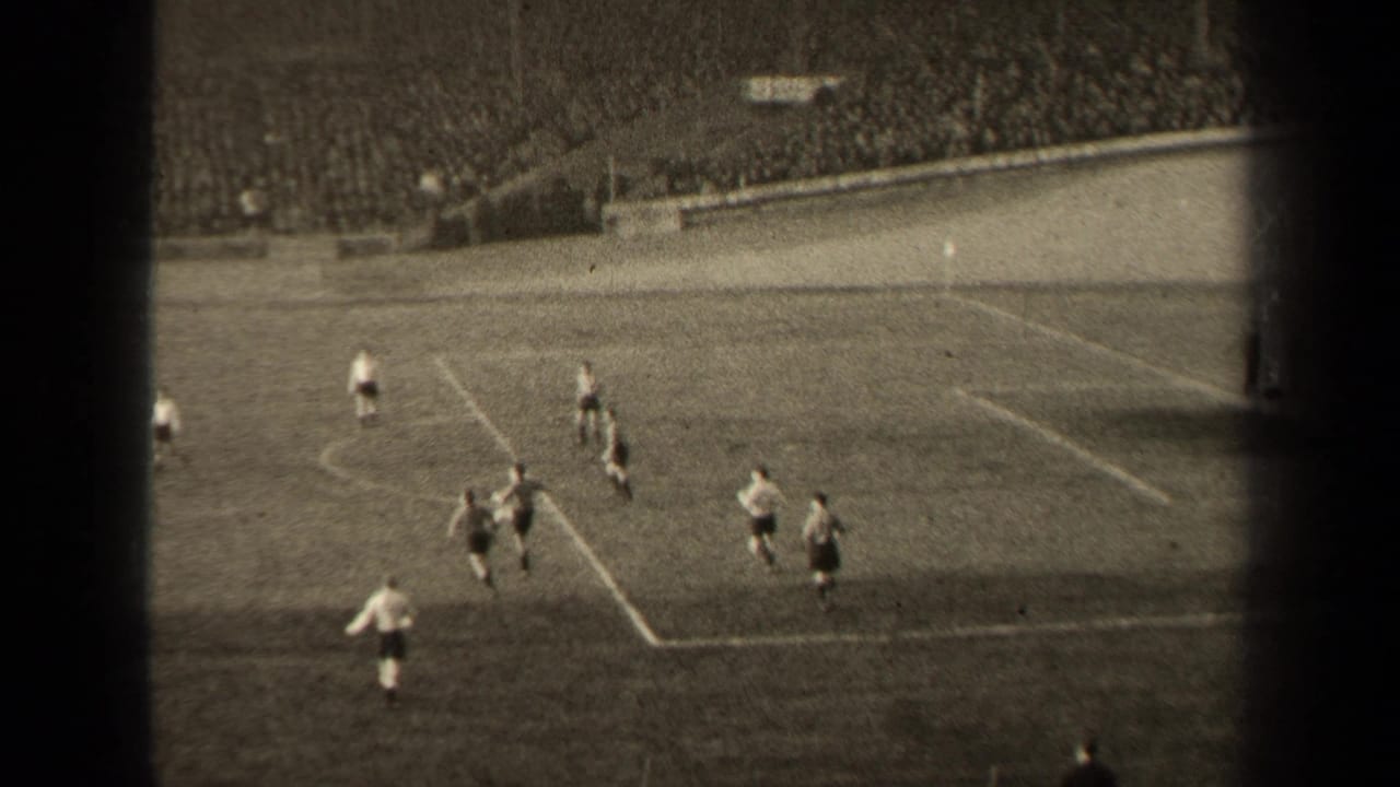 A high-angle 8mm frame shows 1947 Paris soccer players converging near the marked penalty area with spectators filling the stands.