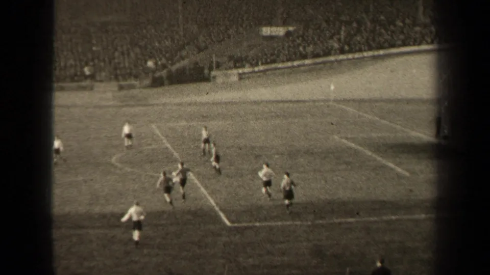 A high-angle 8mm frame shows 1947 Paris soccer players converging near the marked penalty area with spectators filling the stands.