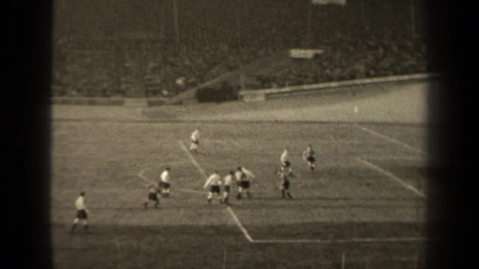 High-angle 1947 Paris stadium view with soccer players gathered near the penalty area and crowded seating in the background.