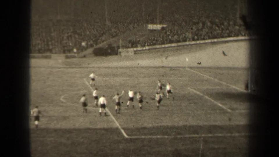 Spectator-shot 1947 Paris soccer scene with players near the box, a dark vertical film edge, and dense stadium seating behind them.