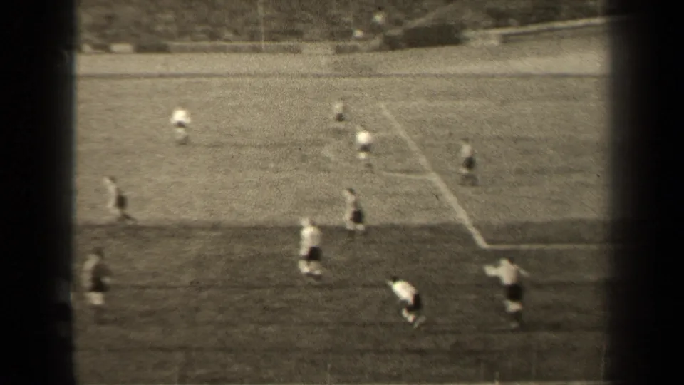 Black-and-white 8mm frame of a 1947 Paris soccer match, with players dispersed across the pitch and stands beyond.