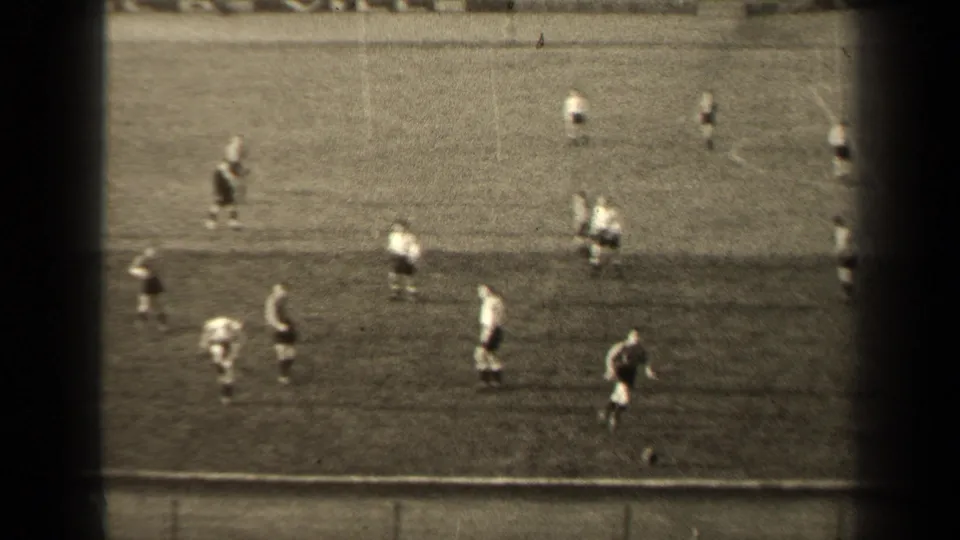 Spectator-view frame from the 1947 Paris match, with several players converging near the touchline on a worn grass pitch.