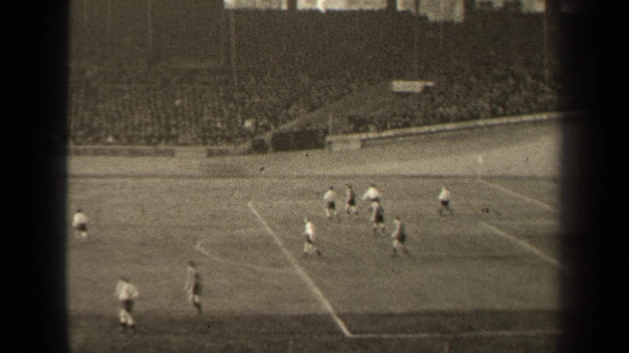 Football players cluster on the pitch with a crowded stadium behind them.
