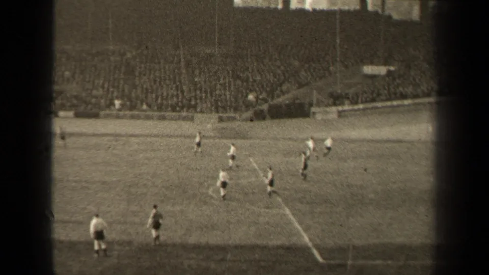 Spectator-shot 1947 Paris football footage with players near the marked area and a dense crowd in the stands.